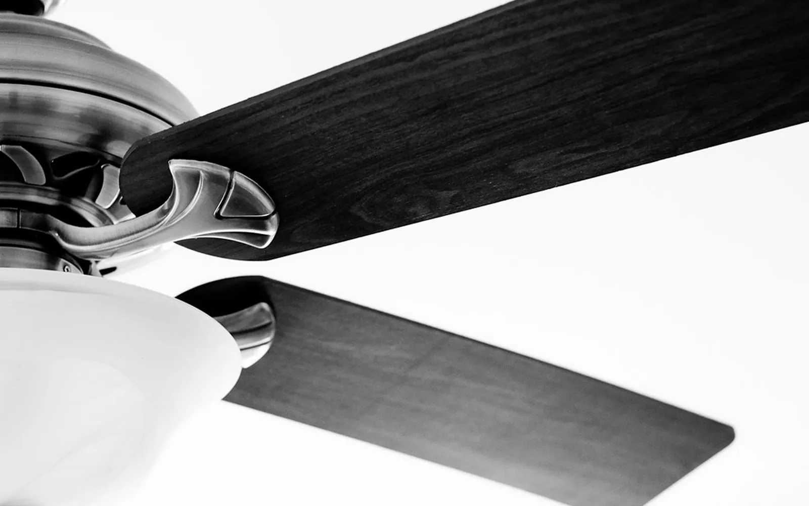 Close-up of a ceiling fan's metal hub and dark wooden blades against a white ceiling