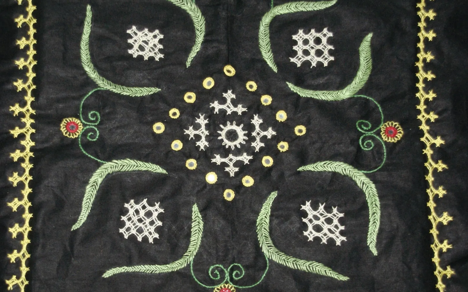 A black cushion cover with colourful hand embroidery in a symmetrical pattern