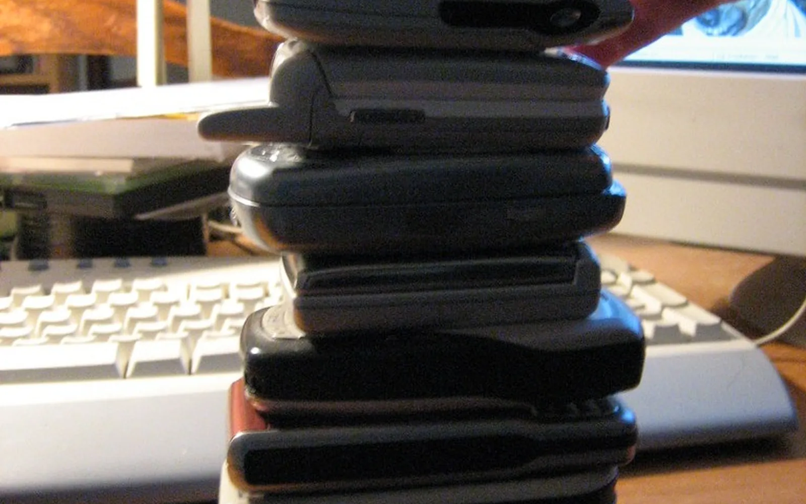 A tall stack of old feature phones and early mobile handsets held by a hand on a wooden desk