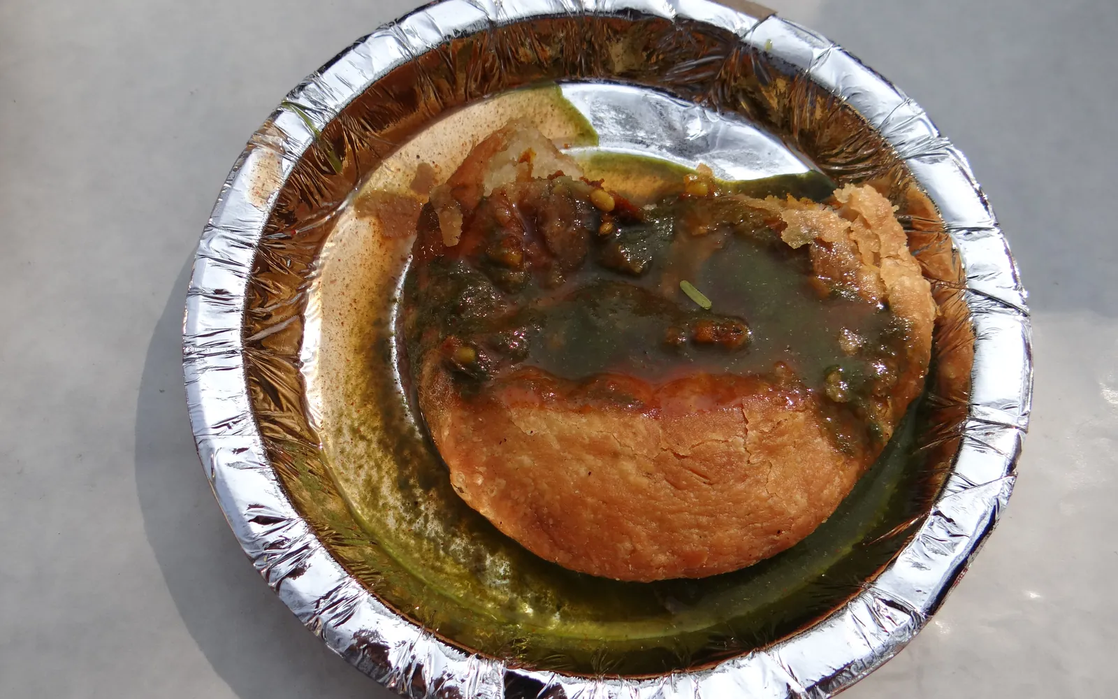 A Rajasthani kachori served on a foil plate with chutney
