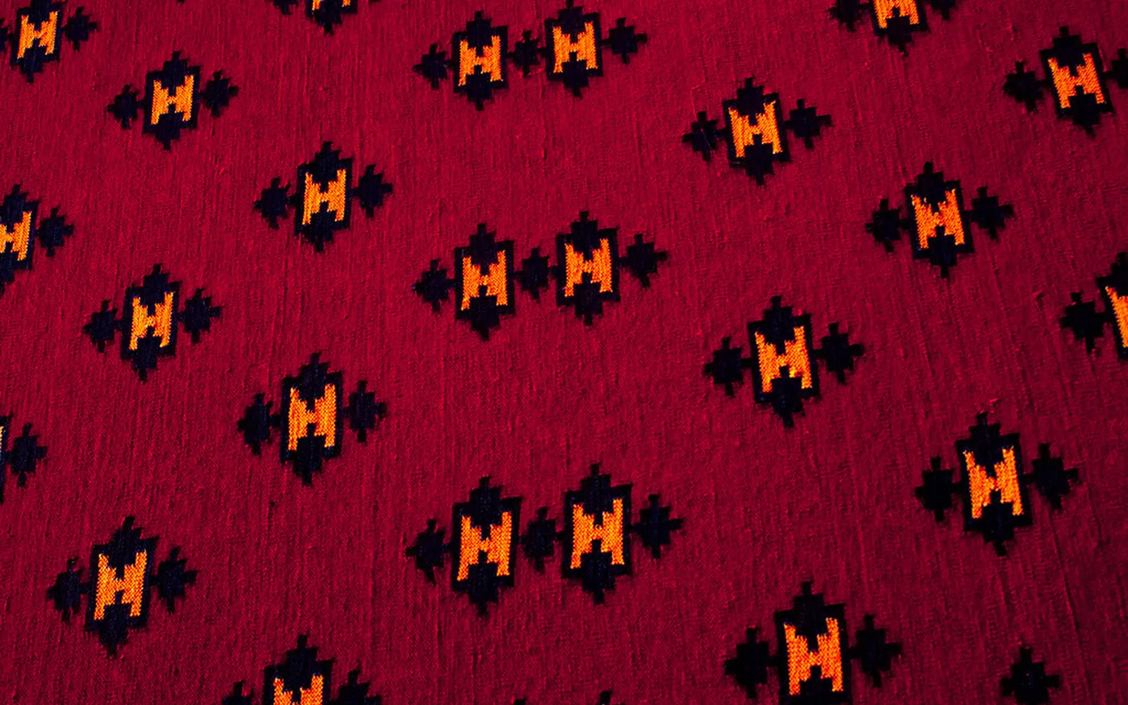 A deep red Rajasthani dhurrie rug with an orange and black geometric pattern