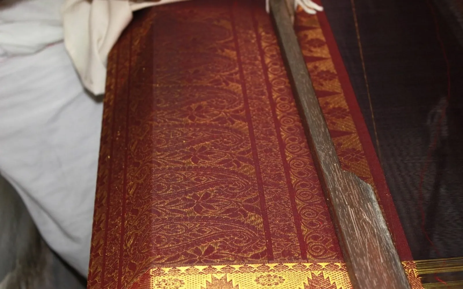 A maroon silk saree with a gold zari border being woven on a handloom
