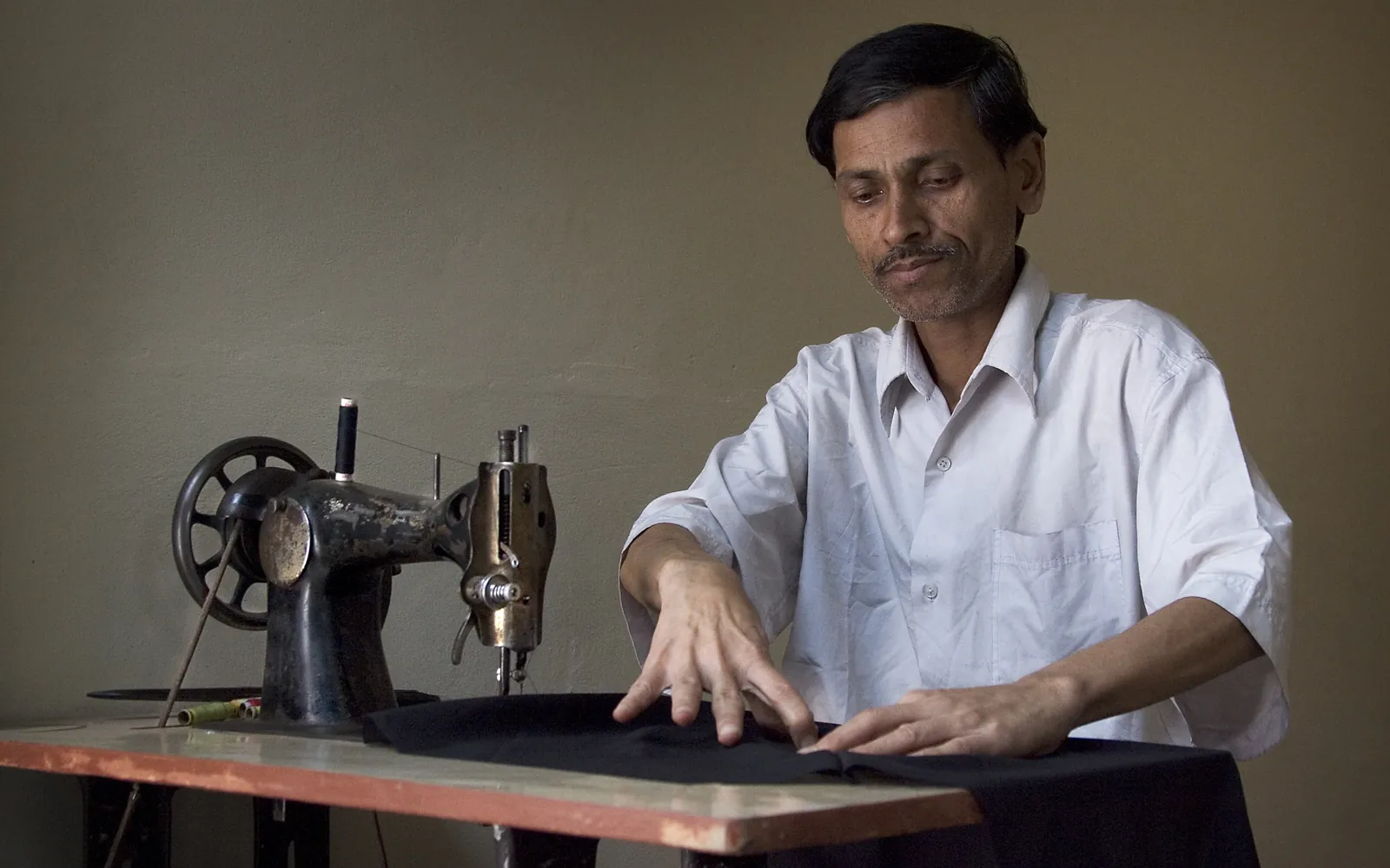 A tailor guiding dark fabric through an old treadle sewing machine